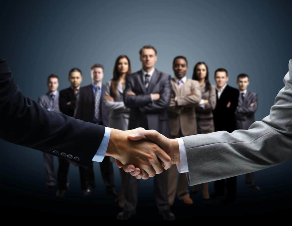 Business professionals shaking hands in front of a team, representing a joint development agreement.