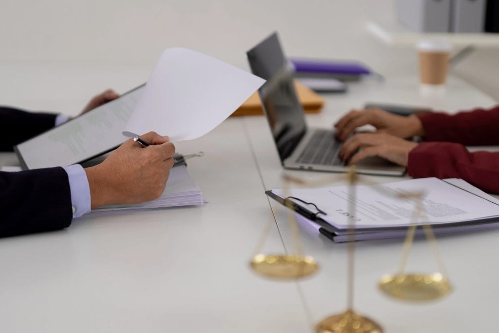 Mediation and arbitration meeting with legal documents, laptop, and scales of justice on a conference table.